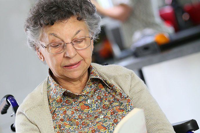 Seniorin im Rollstuhl liest Buch