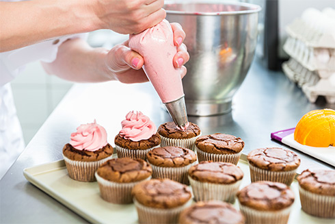 Bäckerin verziert Cupcakes mit einer rosafarbenen Creme 
