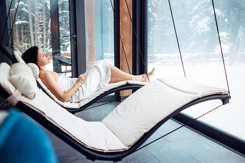 Eine Frau relaxt im Hotel auf einer Liege und genießt den Ausblick aus dem großen Fenster