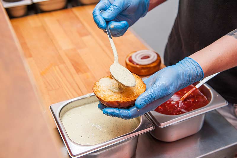 Koch bestreicht Burgerbrötchen mit Mayonnaise